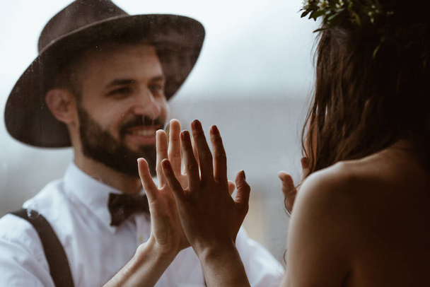 portrait of a stylish wedding couple: Young bearded man in hat and brunette bride in elegant gown wearing a wreath braided in hairstyle - 写真・画像