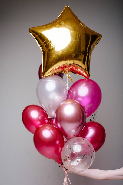 Composition of white, pink, transparent helium balloons and gold star in the hand of a woman on a light background. - Fotoğraf, Görsel