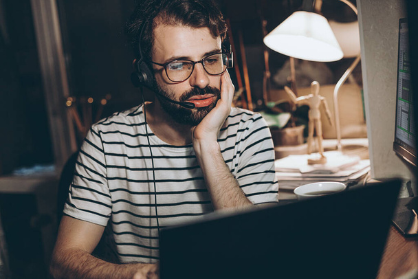 adult bearded man working sitting at home desk at computer, working online. Self-isolation during quarantine, work at home, copy space - Foto, Imagen