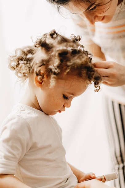 parents unwrap the baby's hair, which they tried to make curly with the help of homemade curlers Home family fun parents with baby. - Photo, image