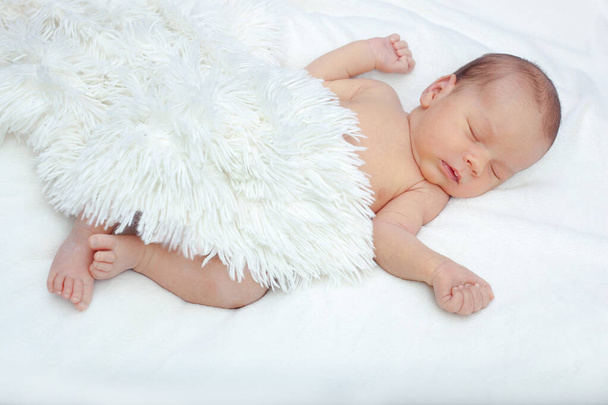 The newborn sleeps under a white fluffy blanket. The lovely newborn is sleeping peacefully. The baby is lying on his back with his hands raised up under a fluffy blanket. - Φωτογραφία, εικόνα
