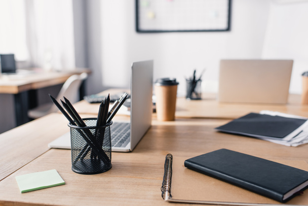 Selectieve focus van notebooks, schrijfwaren en laptops op houten tafel in kantoor  - Foto, afbeelding