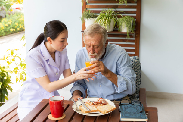 Sairaanhoitaja auttaa vanhempi mies aamiaista yhdessä - Valokuva, kuva