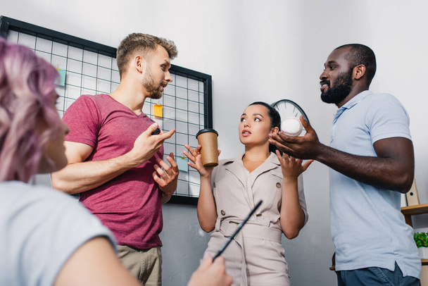 Selektivní zaměření mladých multietnických podnikatelů s kávou jít, baseball míč a pero mluvit v kanceláři  - Fotografie, Obrázek