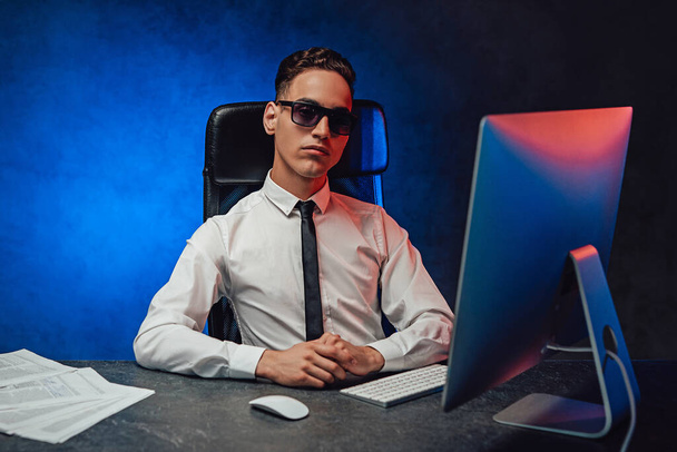 Fiducioso giovane uomo d'affari in camicia bianca e occhiali da sole seduto alla scrivania dell'ufficio - Foto, immagini