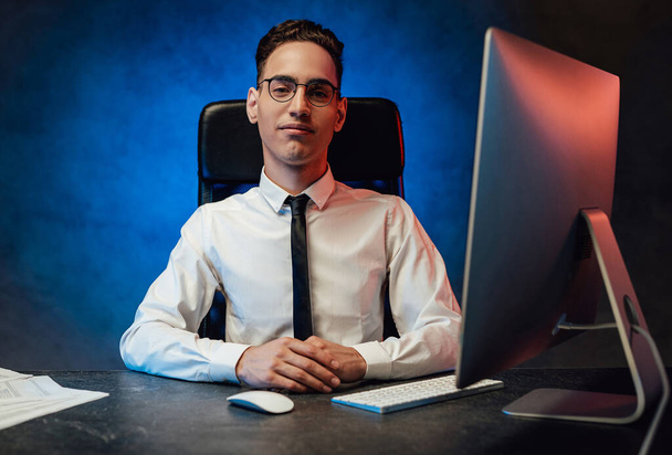 Un giovane impiegato in camicia bianca e cravatta si siede sul posto di lavoro - Foto, immagini