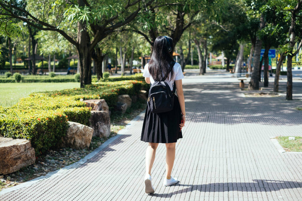 Noir cheveux longs collège fille en uniforme marche sur le chemin dans le parc serein. - Photo, image