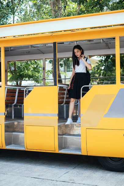Black long hair college girl in uniform walk down the bus, get out of the yellow bus. - Photo, Image