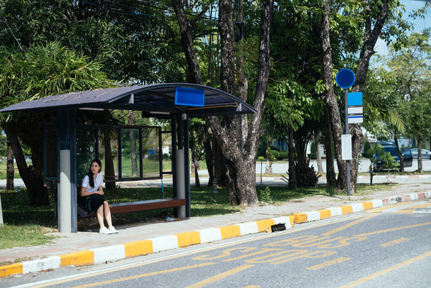 czarny długie włosy studia dziewczyna w mundurze siedzi na przystanek autobusowy czeka na autobus. - Zdjęcie, obraz
