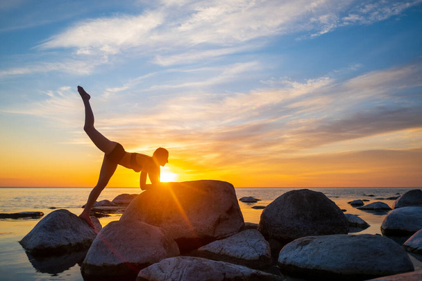 Schlanke Frau macht Yoga gegen strahlenden Sonnenuntergang - Foto, Bild