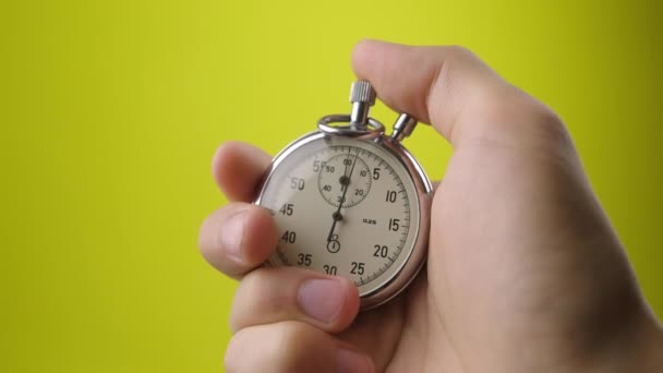 Male hand holding analogue stopwatch on yellow background. Time start with old chronometer man presses start button in the sport concept. Time management concept. - Footage, Video