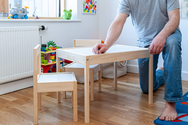 Родитель, собирающий из плоской упаковки набор из двух маленьких стульев со столом в детской спальне. - Фото, изображение