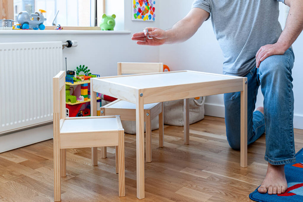 Egy szülő összeszereli a lapos csomagból a két kis széket íróasztallal a gyerekszobában. - Fotó, kép
