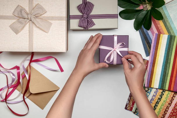 All things for gift wrapping by female hands on white background. Present box with bow. Ribbon and color paper. - Zdjęcie, obraz