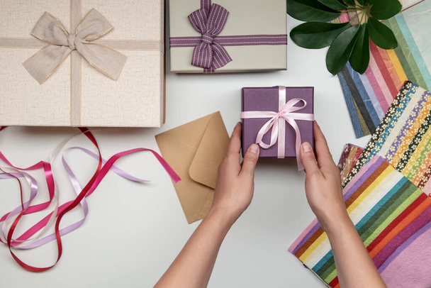 All things for gift wrapping by female hands on white background. Present box with bow. Ribbon and color paper. - Фото, изображение