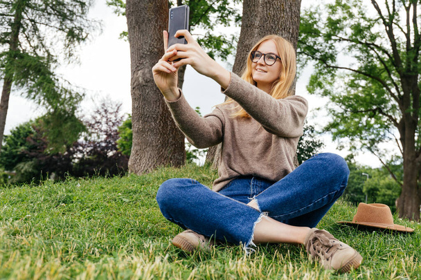 Mooie jonge hippe vrouw die selfie neemt in het publieke park. Ik kijk naar de camera en lach. Reizen en actief leven. - Foto, afbeelding