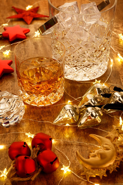 Verre en cristal de whisky et une carafe en cristal de whisky avec lumières de Noël et décorations de cloche de Noël, sur une table en bois - Photo, image