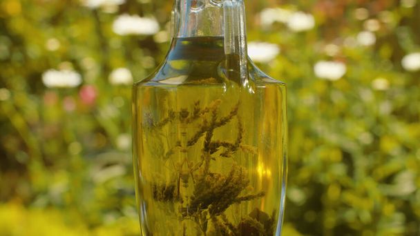 Zamknąć oliwę z oliwek aromatycznymi ziołami w szklanym dzbanku. Butelka na rozmytym naturalnym tle w ogrodzie w letni dzień. Koncepcja zdrowego stylu życia - Zdjęcie, obraz