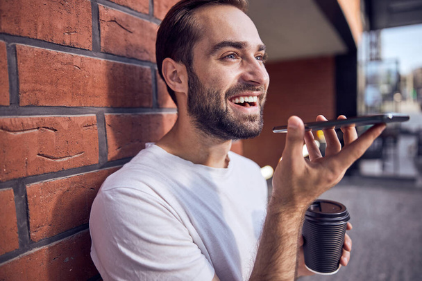 Sonriente hombre guapo hablando en el teléfono inteligente con café - Foto, imagen