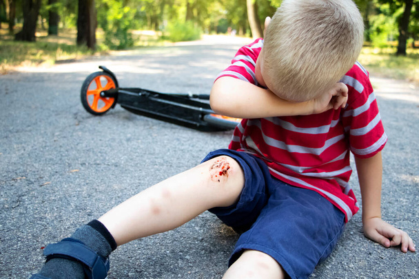 Un garçon de quatre ans est tombé d'un scooter et s'est cassé le genou. Papa fournit les premiers soins en désinfectant la plaie et en appliquant un plâtre. - Photo, image