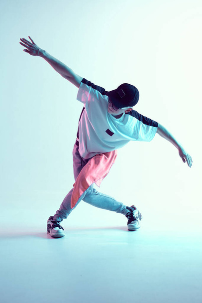 Guy dancing contemporary dance in studio. Neon light blue background. Acrobatic bboy dancer. Break dance lessons. - Foto, imagen