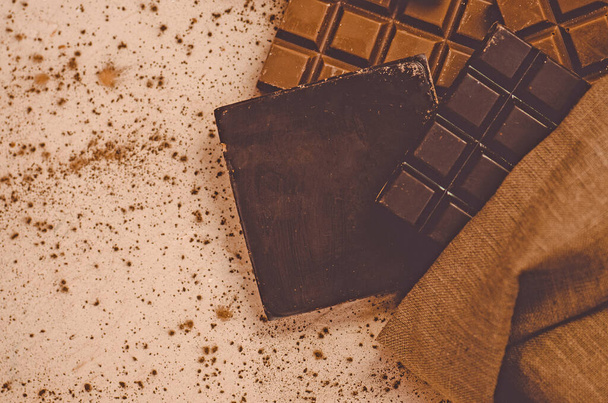 Chocolate candy bars. Chocolate bar pieces in burlap bag. Different milk and dark chocolate. Chocolate pieces on wooden background - Fotoğraf, Görsel
