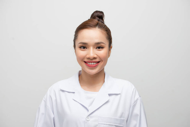 Young doctor woman wearing coat standing over isolated white background with a happy and cool smile on face. - Фото, изображение