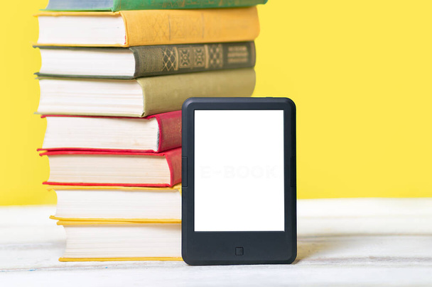 Leggo. E-book reader e una pila di libri su sfondo giallo. Scherza. Concetto di educazione e gadget elettronici. - Foto, immagini
