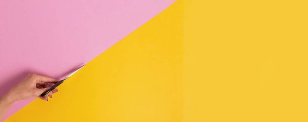 The left female hand cuts the pink-yellow background in half with scissors. International Left-handers Day on August 13 - 写真・画像