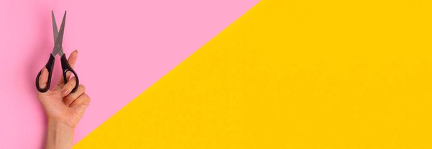 Las tijeras están en la mano izquierda de la mujer. Banner en rosa brillante y amarillo, partido por la mitad. Día Internacional de la Izquierda el 13 de agosto - Foto, Imagen