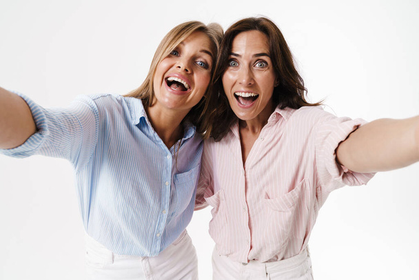 Image of delighted nice two women hugging while taking selfie photo isolated over white background - 写真・画像