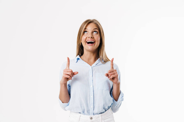 Imagen de mujer rubia feliz apuntando con los dedos hacia arriba y sonriendo aislada sobre fondo blanco - Foto, Imagen