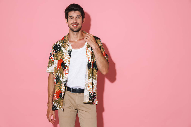 Portrait of cheerful young man in flamboyant shirt smiling and posing on camera isolated over pink background - Foto, afbeelding