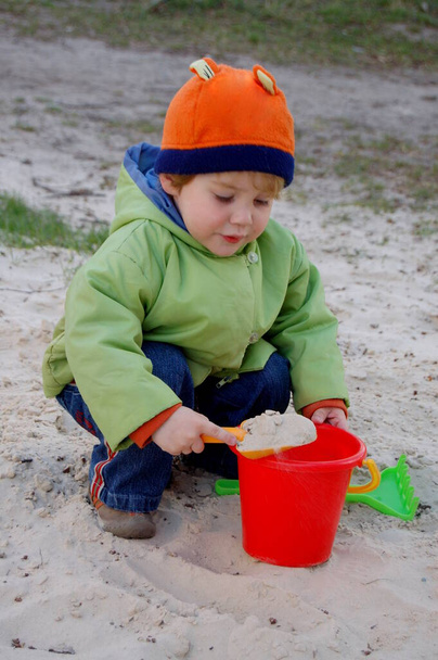 Mały chłopiec bawiący się w parku w piaskownicy w jasnych ubraniach - Zdjęcie, obraz