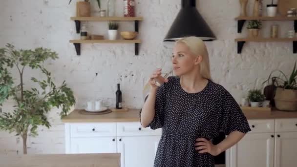 The girl drinks water from a glass standing in the bright kitchen. - Záběry, video
