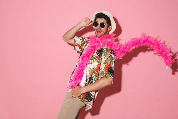 Portrait of cheerful young man wearing boa dancing and smiling isolated over pink background - Fotoğraf, Görsel