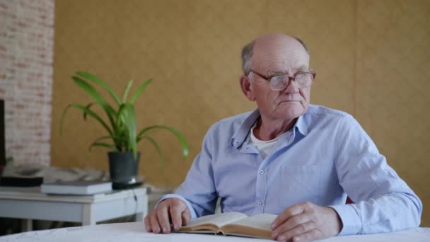 családi kapcsolat, aranyos gondoskodó férfi gyermek üveg tiszta ivóvíz szeretett idős nagyapa szemüveg látvány olvasás közben könyvet, miközben ül az asztalnál a szobában - Felvétel, videó