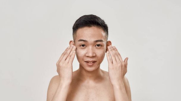 Refresque. Retrato de jovem asiático sem camisa enxaguando o rosto depois de barbear olhando para a câmera isolada sobre fundo branco. Beleza, conceito de rotina de cuidados da pele
 - Foto, Imagem