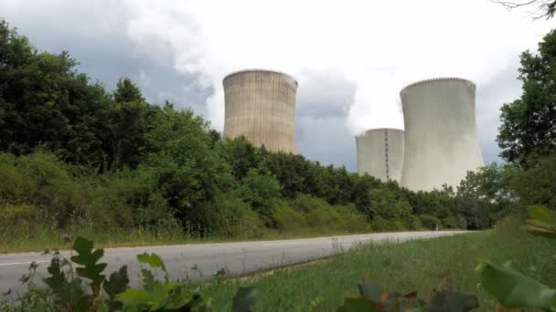 Polttava ydinvoimala puiden takana, edessä lehtien peittämä tie - Materiaali, video
