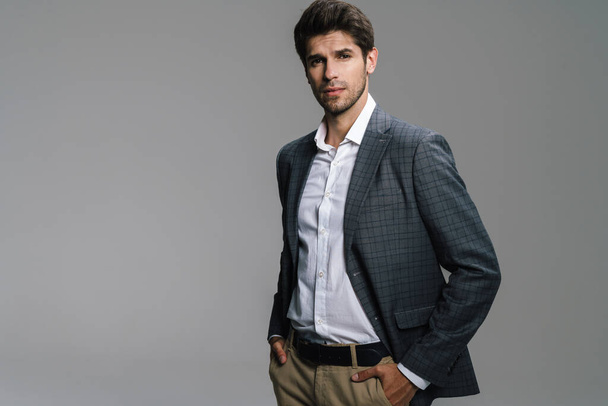 Photo of respectable confident businessman in jacket posing and looking at camera isolated over grey wall - Fotografie, Obrázek