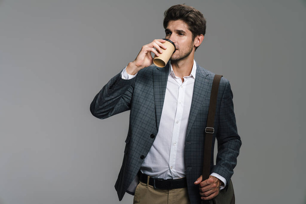 Photo of respectable confident businessman with bag drinking coffee takeaway isolated over grey wall - Φωτογραφία, εικόνα