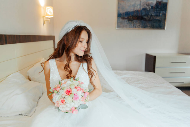 Утро невесты в розовом халате и вуаль в отеле на кровати, свадебное платье - Фото, изображение
