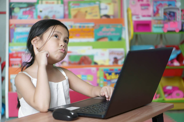 Asiático niño nueva idea pensar o niña feliz estudio en línea o trabajar desde casa o permanecer en la computadora portátil o jugar portátil por la escuela de kindergarten a la educación primaria de coronavirus covid-19 flagelo - Foto, imagen