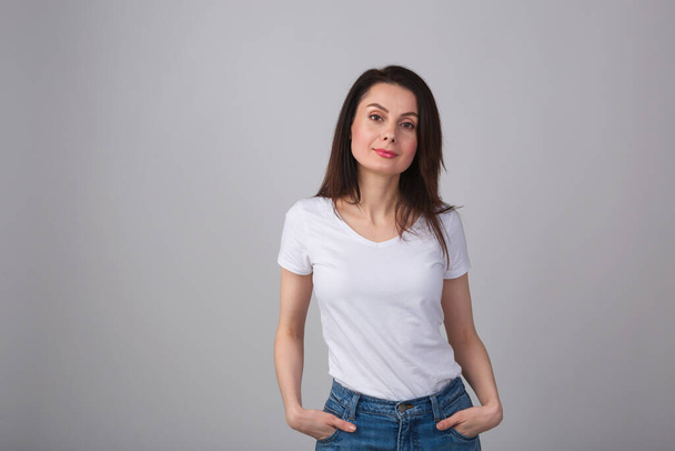 Beautiful young woman in casual clothes.Pretty white girl in 30s wearing classic blue jeans,white t-shirt,red lipstick in studio posing with cheerful smile.Attractive female model smiling in camera - Φωτογραφία, εικόνα