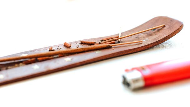 Burnt aromatic sticks on a brown wooden stand next to a lighter - Foto, imagen