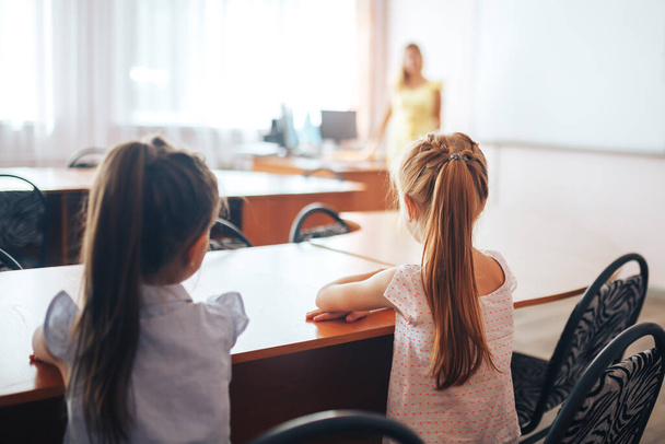 Dos colegialas se sientan en un escritorio en una clase escolar y escuchan atentamente al maestro. - Foto, imagen