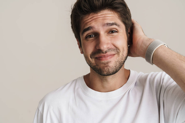 Portrait of pleased unshaven man in basic t-shirt smiling and looking at camera isolated over white background - Фото, изображение