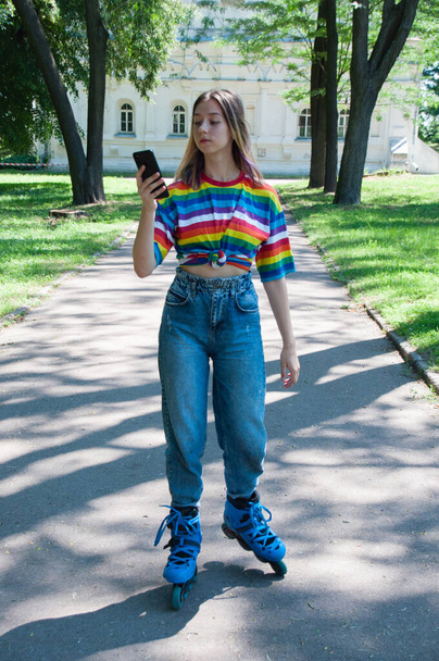 Очень красивая девушка на роликовых коньках в наушниках, со смартфоном в городском парке, слушая музыку или разговаривая - Фото, изображение