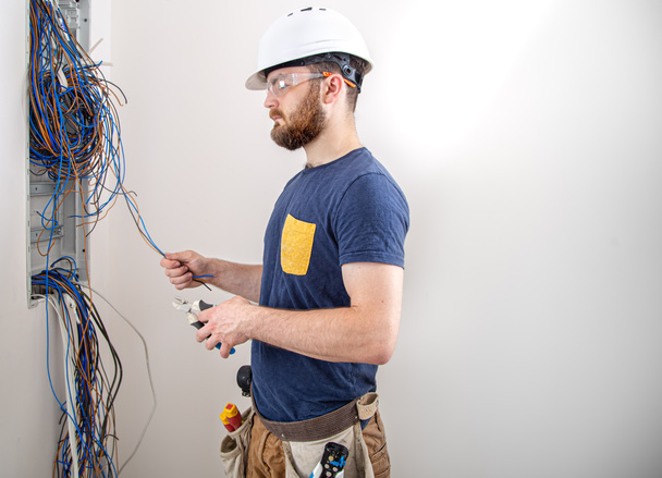 Electrician Builder at work, examines the cable connection in the electrical line in the fuselage of an industrial switchboard. Professional in overalls with an electrician's tool. The concept of working as a professional. - Photo, Image