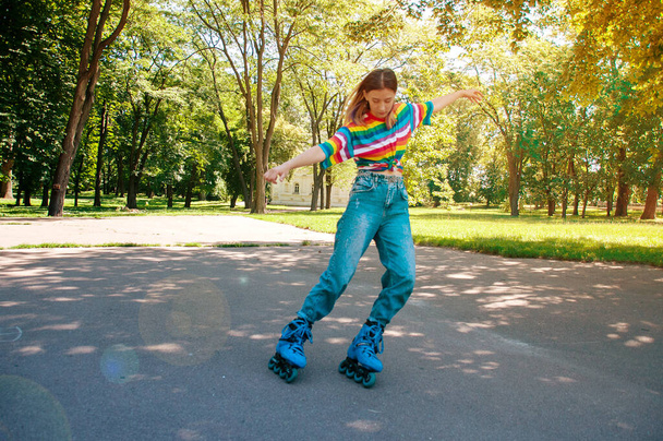 Beautiful teenager girl performs tricks on roller skates in the park on summer sunny day - Photo, Image